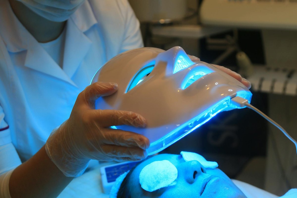 Beautician applying LED red light therapy face mask during a relaxing spa treatment